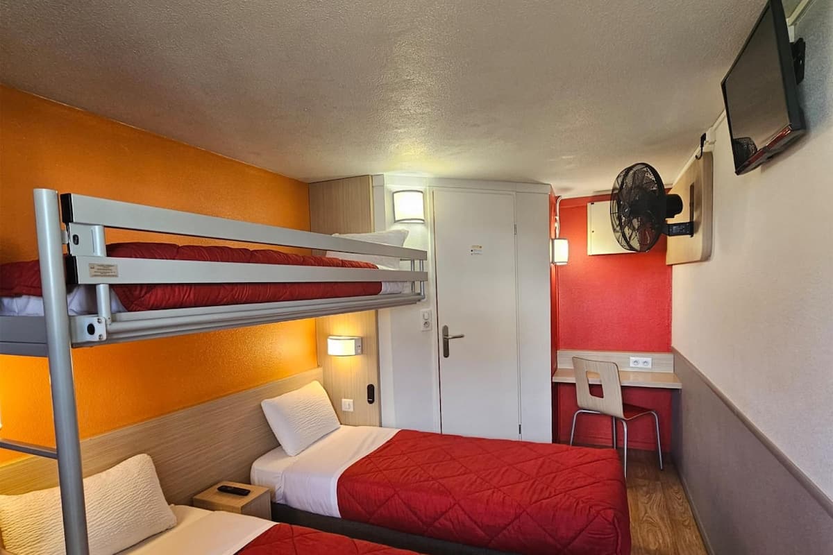 A compact room with bunk beds, a desk, a chair, and a TV mounted on the wall.