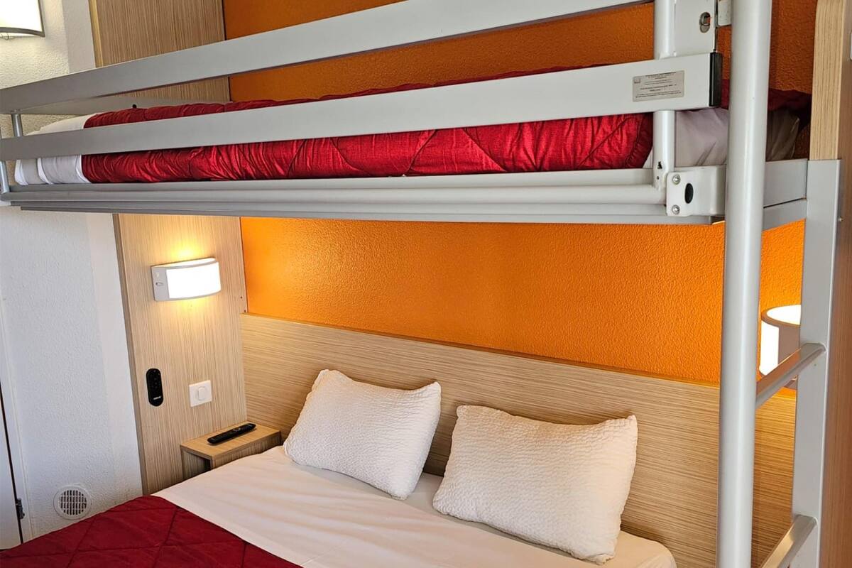 A bunk bed with a red quilt, white pillows, and a wooden headboard.