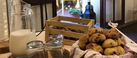 Een kamer met een houten tafel waarop een kruik melk, een mandje koekjes en een schaal met eten staan.