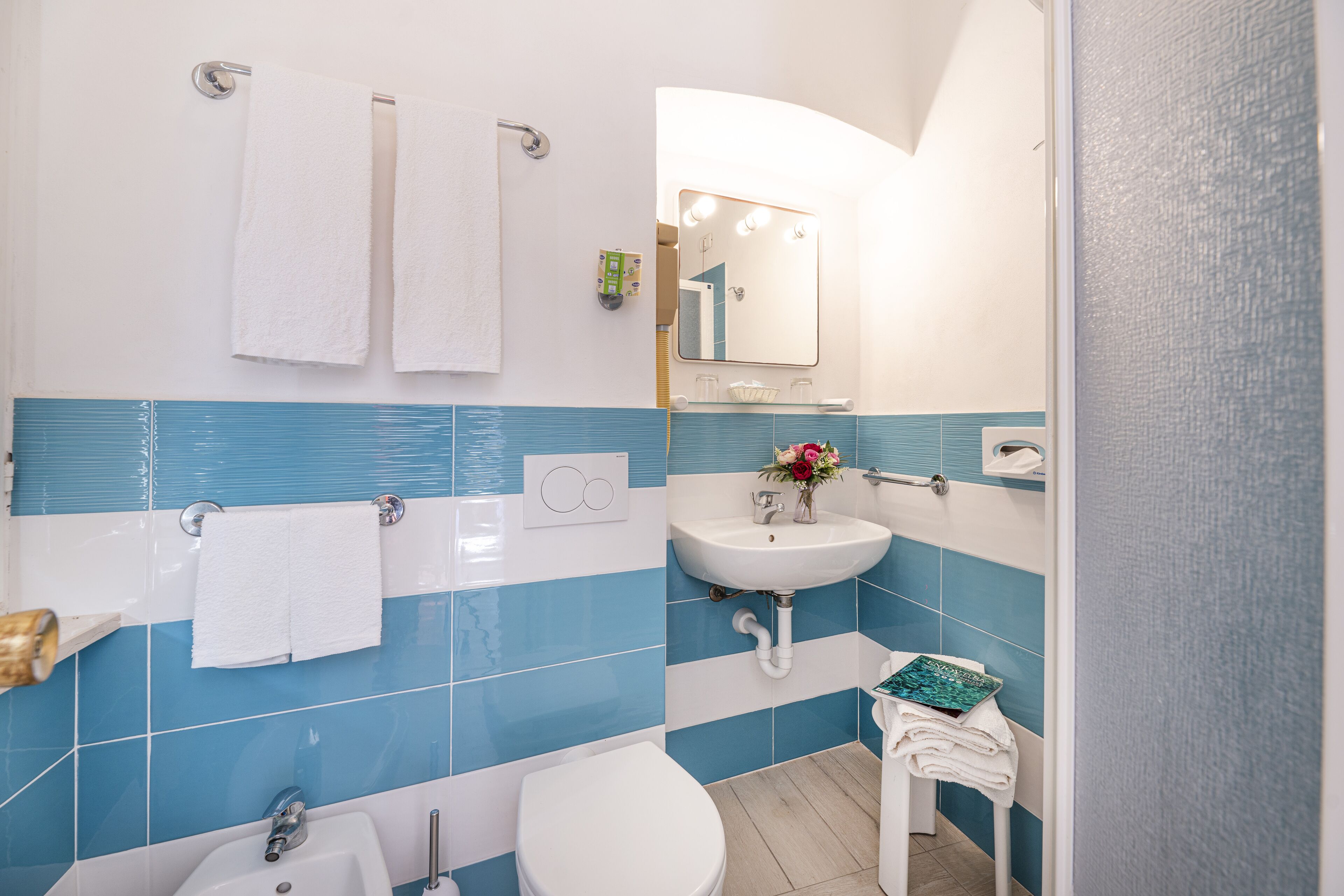 Ein Badezimmer mit einem weißen Waschbecken, einer weißen Toilette und einer Badewanne. Zwei weiße Handtücher hängen an der Wand.