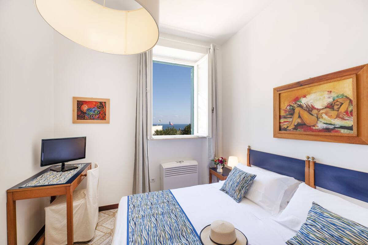 Une chambre d’hôtel avec un lit, un bureau équipé d’un ordinateur, une fenêtre donnant sur un paysage agréable et des œuvres d’art accrochées aux murs.