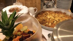 A buffet table with various dishes, including a large fruit bowl, a pie, and a custard dessert.