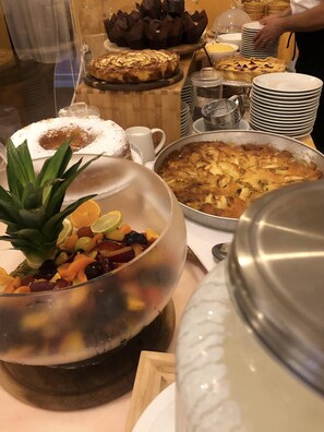 A buffet table with various dishes, including a large fruit bowl, a pie, and a custard dessert.