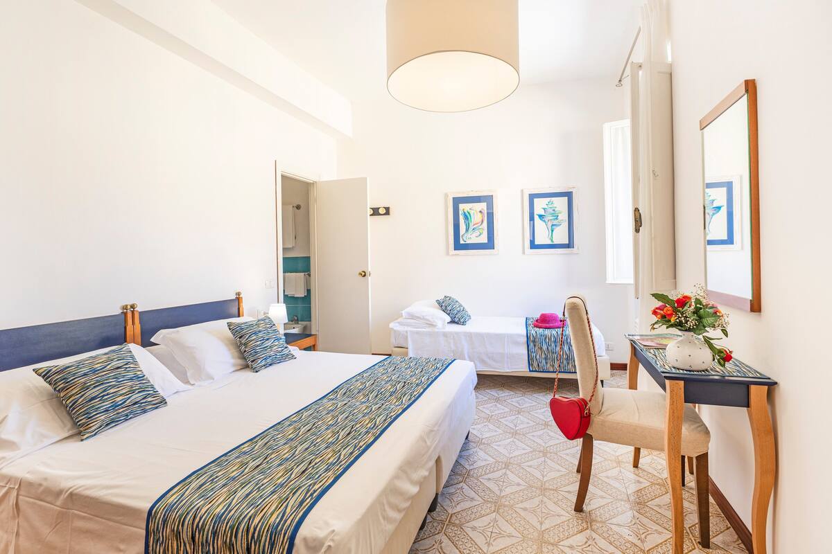 Une chambre d’hôtel avec un grand lit, un bureau avec une chaise, un miroir et des œuvres d’art accrochées aux murs.