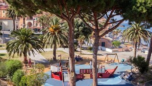 A coastal park with playgrounds, palm trees, and a view of the sea and buildings. - Hotel Rio Sul Mare (Rio)