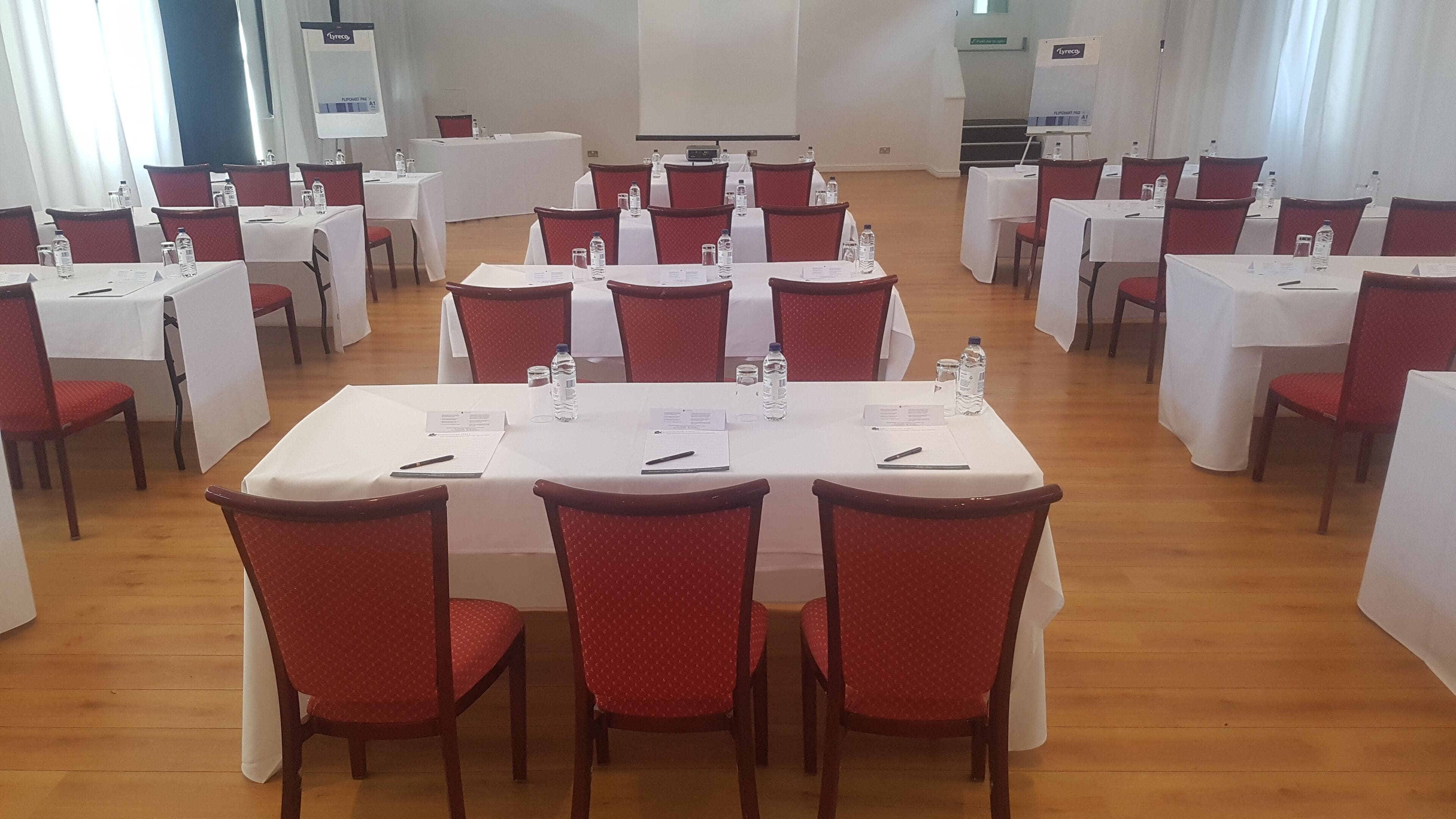 A conference room with multiple tables and chairs, white tablecloths, and water bottles.