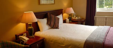 Una camera d'albergo con un letto, due lampade ai comodini, un telefono, una sedia e una finestra con tende.