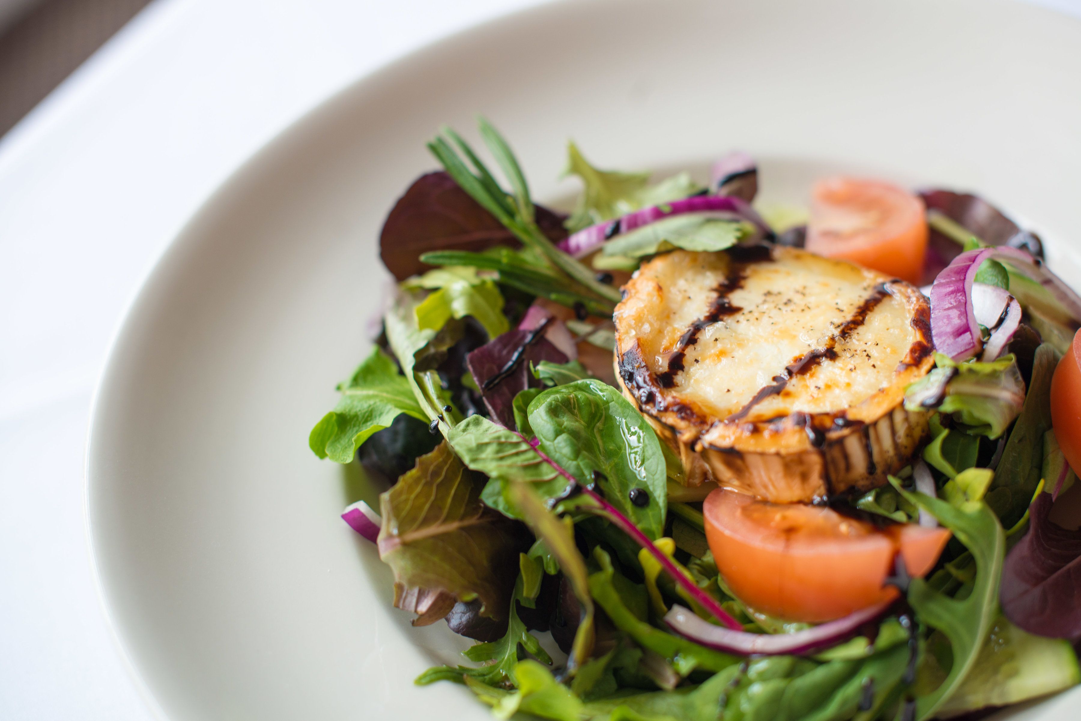 A plate of grilled chicken breast on a bed of mixed greens and sliced tomatoes.