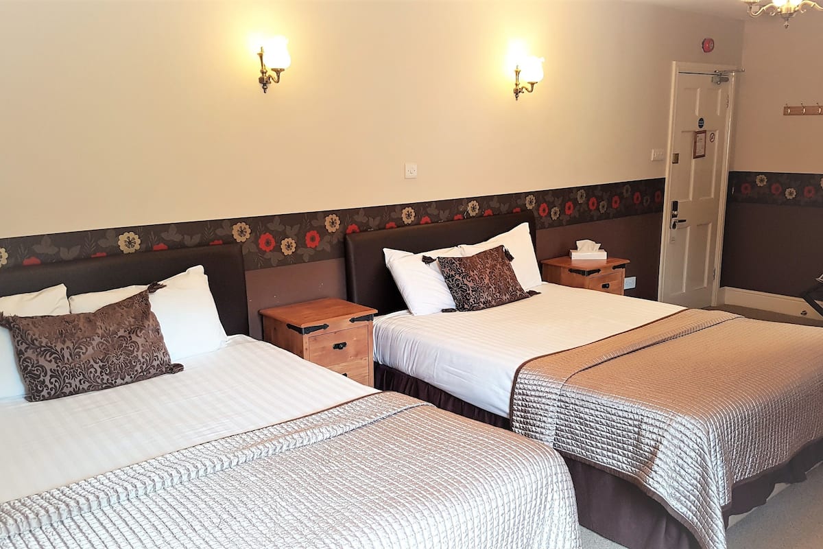 Habitación de hotel con dos camas, cada una con mesita de noche y lámpara de pared.
