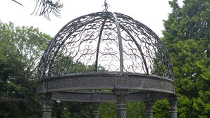 Un gazebo con decorazioni in metallo, immerso in un prato curato e circondato da siepi.