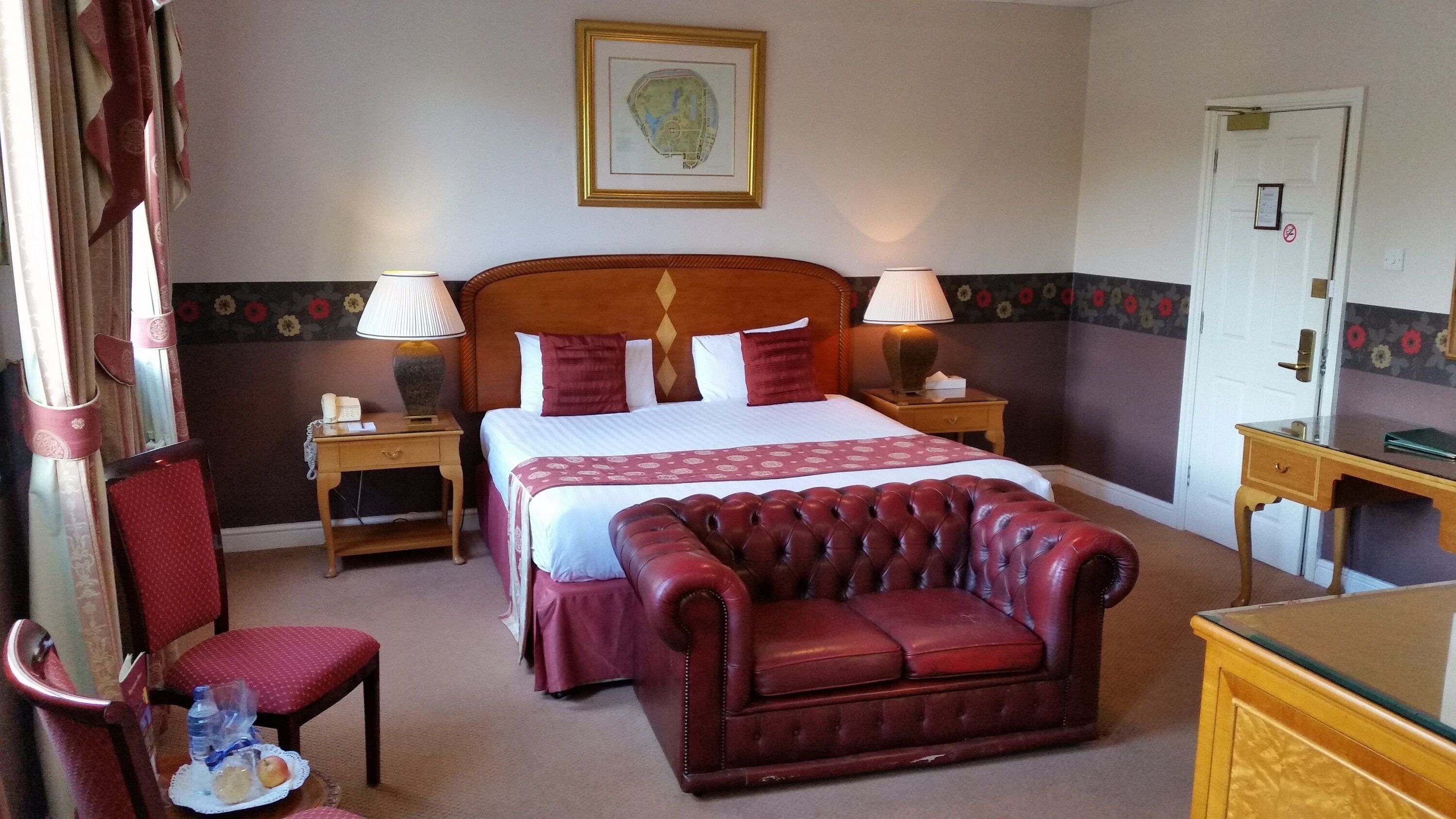 Une chambre d’hôtel avec un grand lit, deux tables de chevet avec des lampes, un canapé en cuir, un bureau en bois et une chaise.