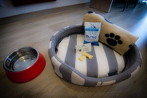 A pet bed with a striped pattern sits on the floor, accompanied by a bowl and dog food.