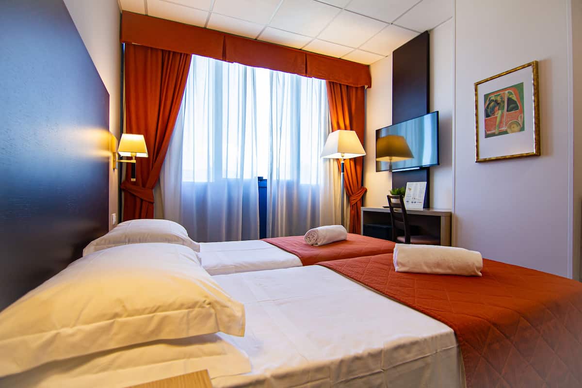 Quarto de hotel com duas camas, uma televisão e um quadro na parede.
