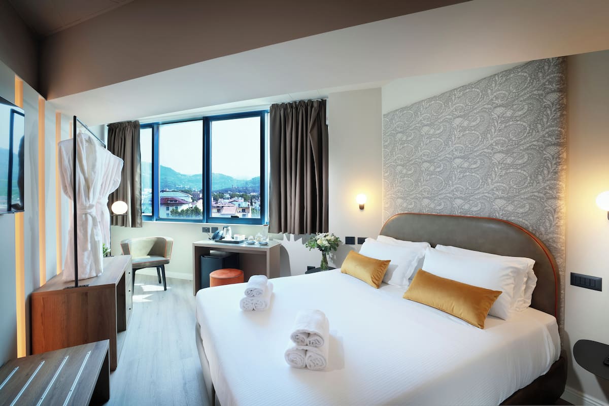 Quarto de hotel com uma cama grande, uma escrivaninha, uma cadeira e vista para a cidade.