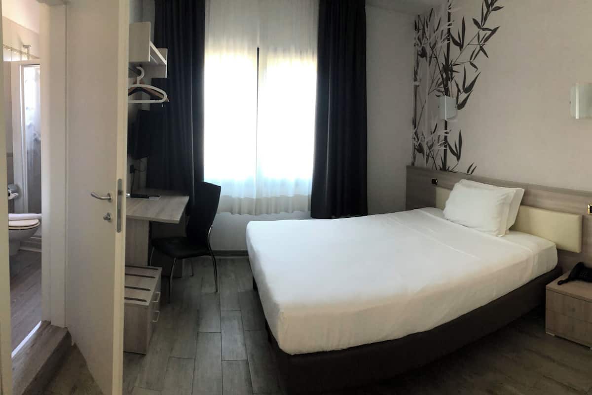 A hotel room with a bed, bedside table, and a small wooden bench.