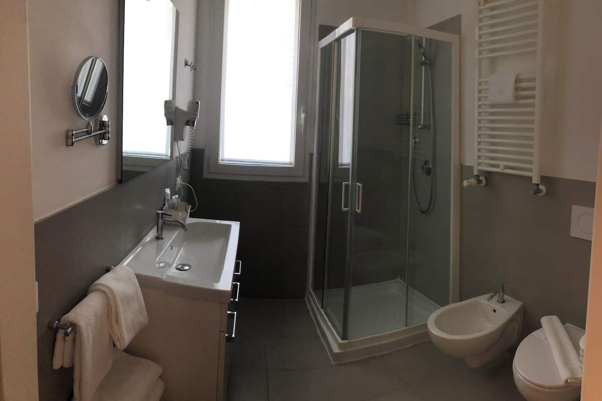 A modern bathroom with a glass shower enclosure, a bidet, and a sink with a mirror.
