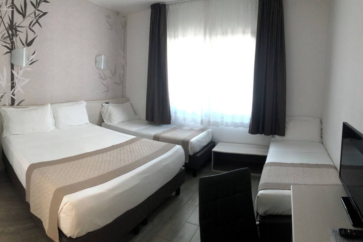 A hotel room with a large bed, a smaller bed, a desk with a laptop, and a TV.