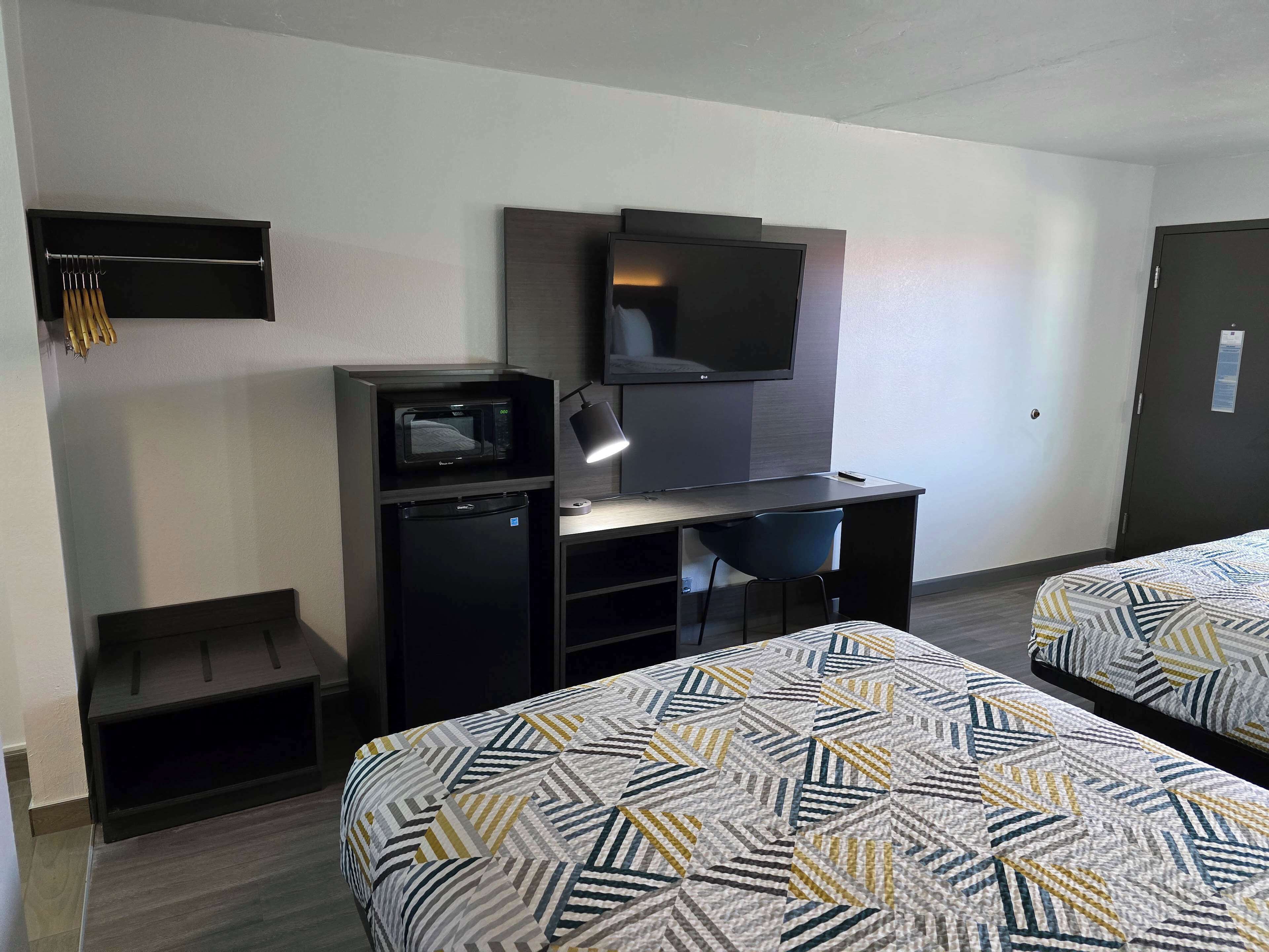 A hotel room with a bed, a desk with a computer, a microwave, and a small refrigerator.