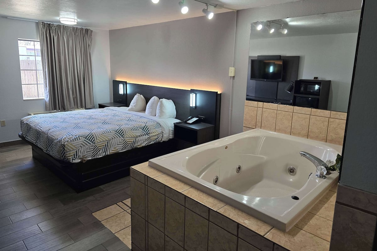 Une chambre d’hôtel moderne dotée d’un grand lit, d’une salle de bain séparée avec baignoire, d’un téléviseur à écran plat et d’un four à micro-ondes.