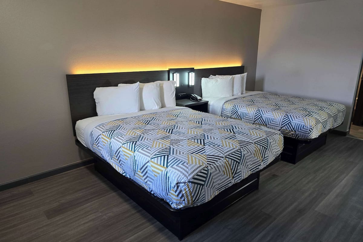 Une chambre d’hôtel avec deux lits, chacun agrémenté de draps à motifs, une table de chevet avec un téléphone et une tête de lit dotée d’un éclairage intégré.