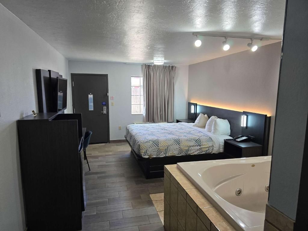 A hotel room with a bed, a desk, a TV, a bathroom with a bathtub, and a window with curtains.