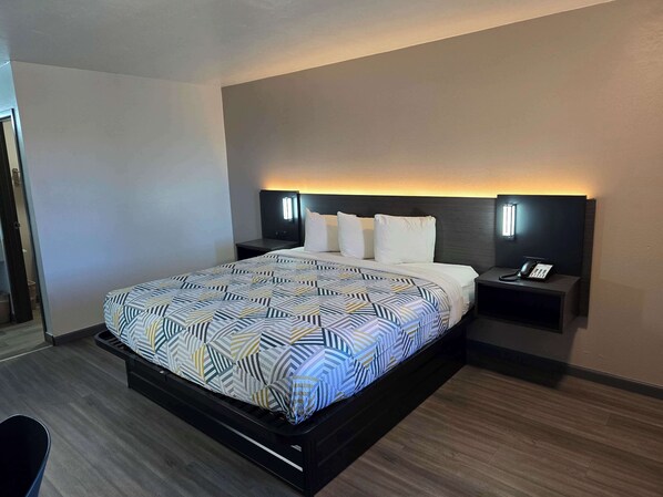 A modern hotel room with a large bed, a bedside table with a phone, and a wall-mounted light.
