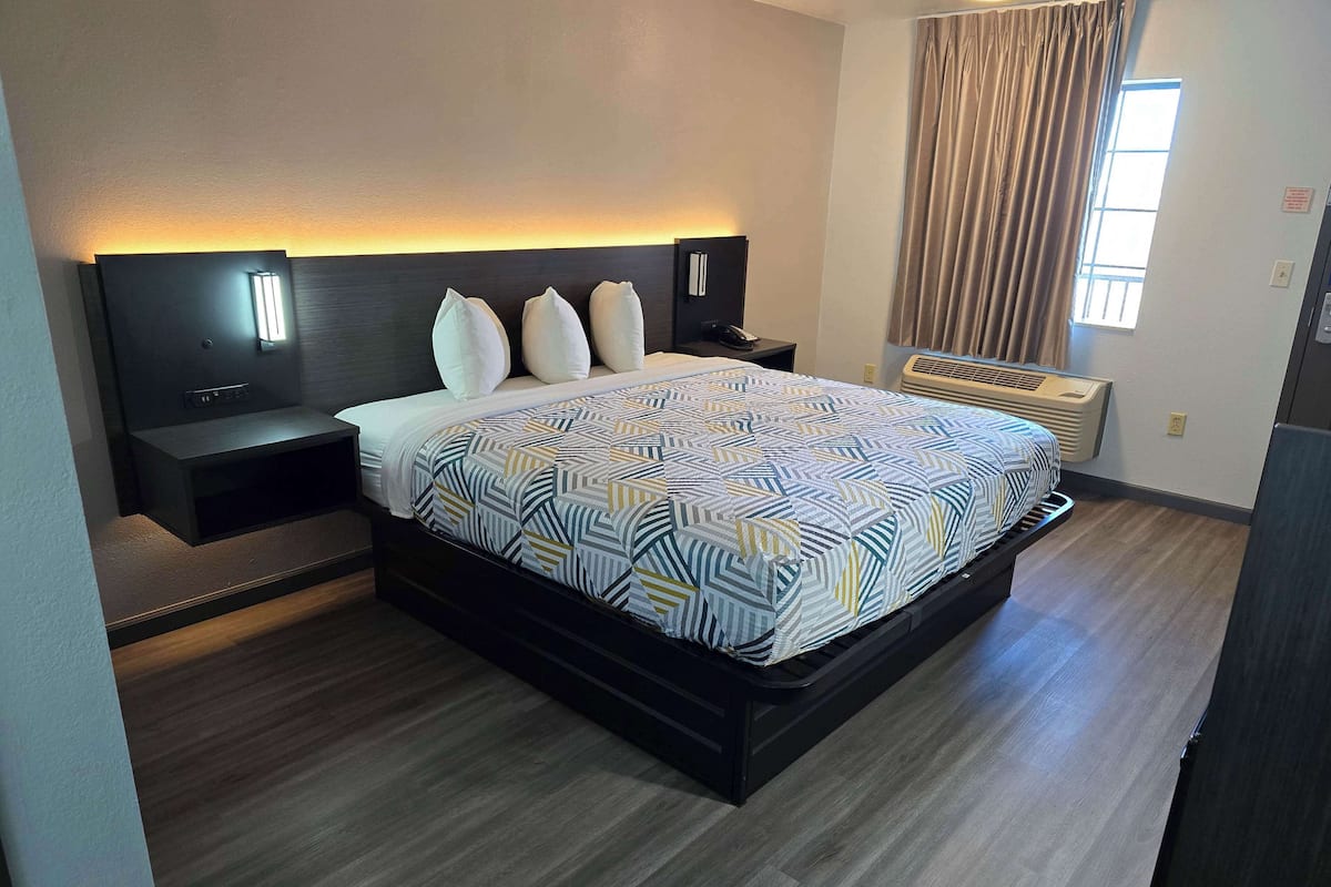 Une chambre d’hôtel moderne dotée d’un grand lit, d’une table de chevet, d’une commode, d’un téléviseur fixé au mur et d’une fenêtre avec des rideaux.