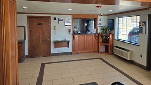 A reception area with a wooden reception desk, a phone, a bulletin board, and a window with a view of parked cars. - Motel 6 Oklahoma City, OK - Frontier City (Oklahoma City)