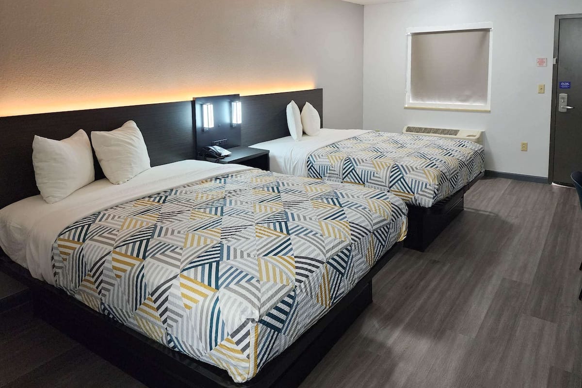 Une chambre d’hôtel avec deux lits, une table de chevet, une fenêtre et une porte.