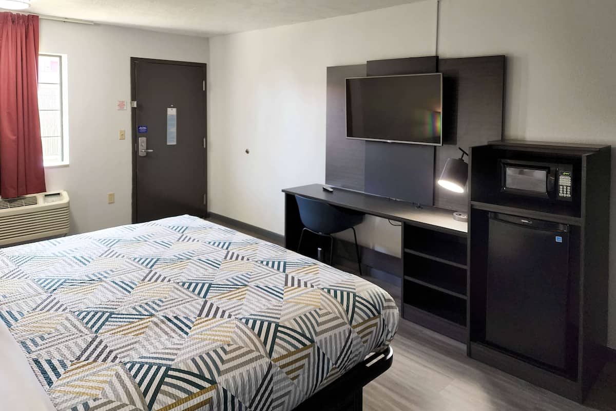 Une chambre d’hôtel équipée d’un lit, d’un bureau, d’une télévision et d’un four à micro-ondes.