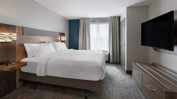 A modern hotel room with a large bed, a flat-screen TV, a bedside table with a lamp, and a window with curtains.