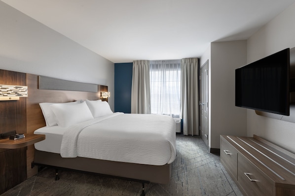 Une chambre d’hôtel moderne dotée d’un grand lit, d’un téléviseur à écran plat, d’une table de chevet avec une lampe et d’une fenêtre avec des rideaux.