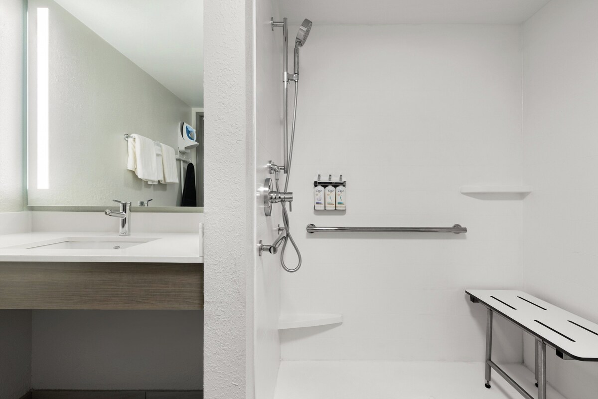 A modern bathroom with a white sink, a mirror, a shower with a handheld showerhead, and a grab bar.