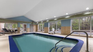 An indoor swimming pool with clear blue water, a lounge area with chairs, and large windows offering a view of the outdoors. - Holiday Inn Express Savannah Airport by IHG (Savannah)