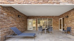 A patio area with a stone wall, a lounge chair, a table with chairs, and a sliding glass door. - Holiday Inn Express Savannah Airport by IHG (Savannah)