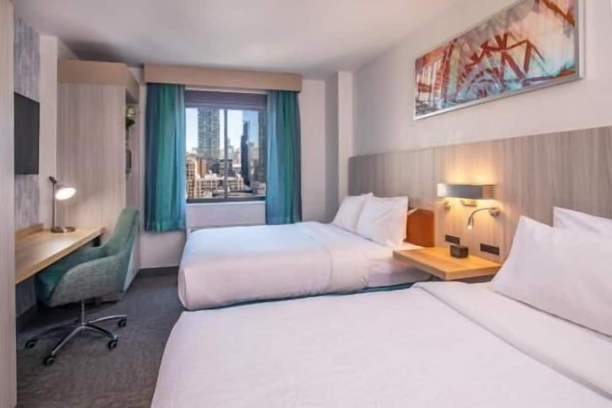 Une chambre d’hôtel avec deux lits, un bureau avec une lampe, une chaise et une fenêtre avec des rideaux.