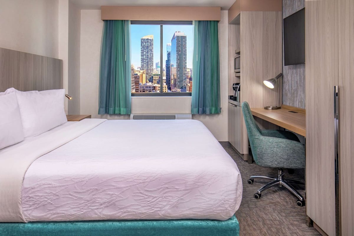 Une chambre d’hôtel avec un grand lit, un bureau, une chaise, une télévision et une fenêtre donnant sur la ville.