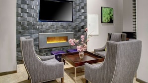 Un salon moderne avec un mur décoré d’un motif imitant la pierre, un téléviseur à écran plat, une cheminée et deux fauteuils rembourrés.