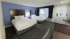 A hotel room with two beds, a desk, and a window with curtains. - Beacon Inn and Suites (Lincoln)