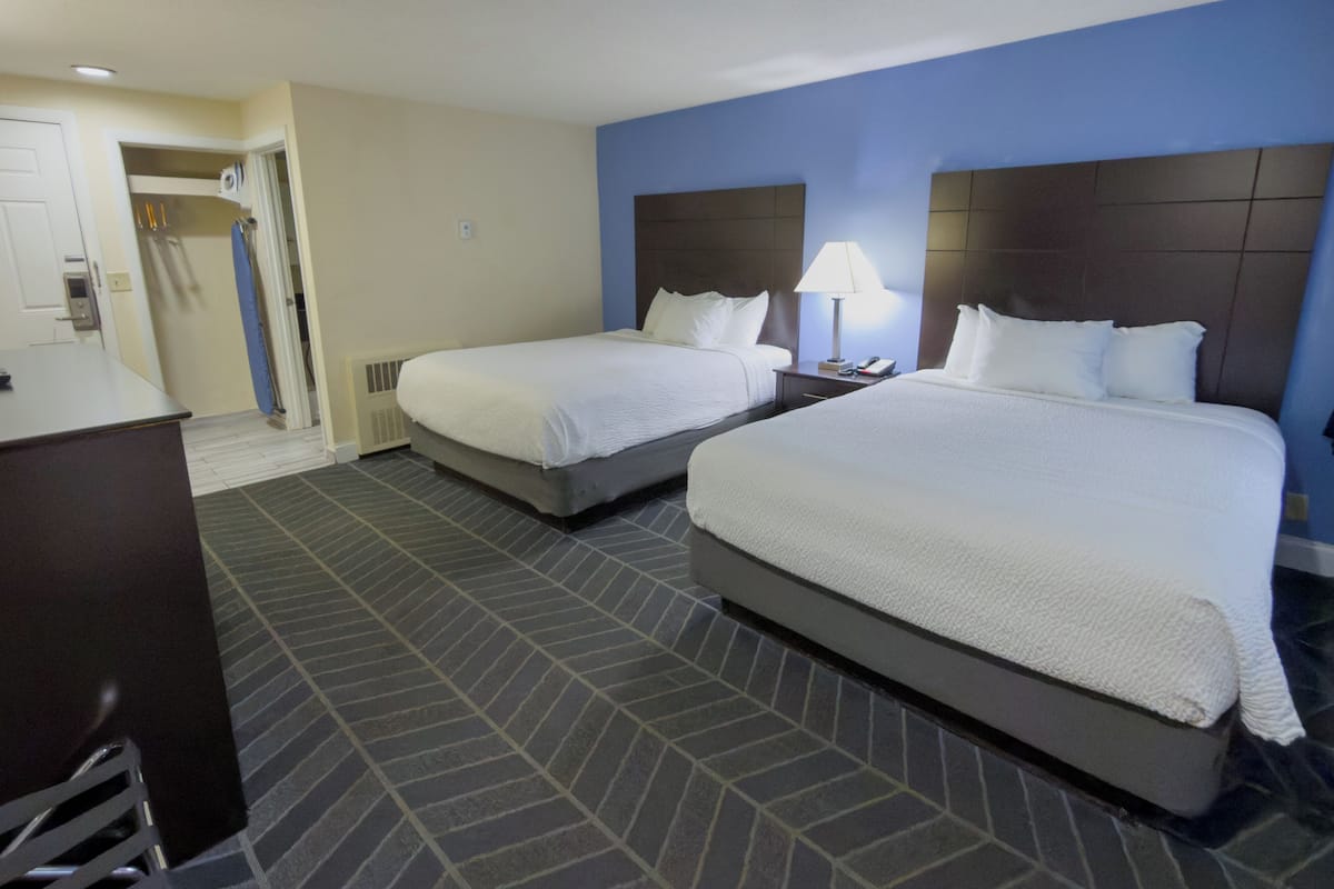 A hotel room with two beds, a desk, a chair, a lamp, and a door leading to a bathroom.