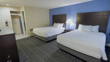 A hotel room with two beds, a desk, a chair, a lamp, and a door leading to a bathroom.