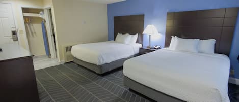 A hotel room with two beds, a desk, a chair, and a bathroom.
