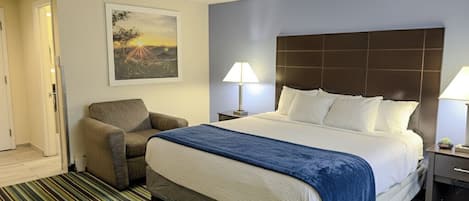 A hotel room with a large bed, a chair, a nightstand, and a painting on the wall.