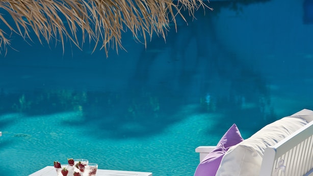 Un espace aménagé au bord de la piscine, avec une table et des chaises longues, donnant sur une piscine à l’eau d’un bleu limpide.