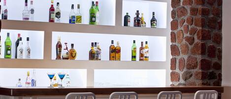 A bar area with multiple shelves of liquor bottles, a brick wall, and four white chairs.