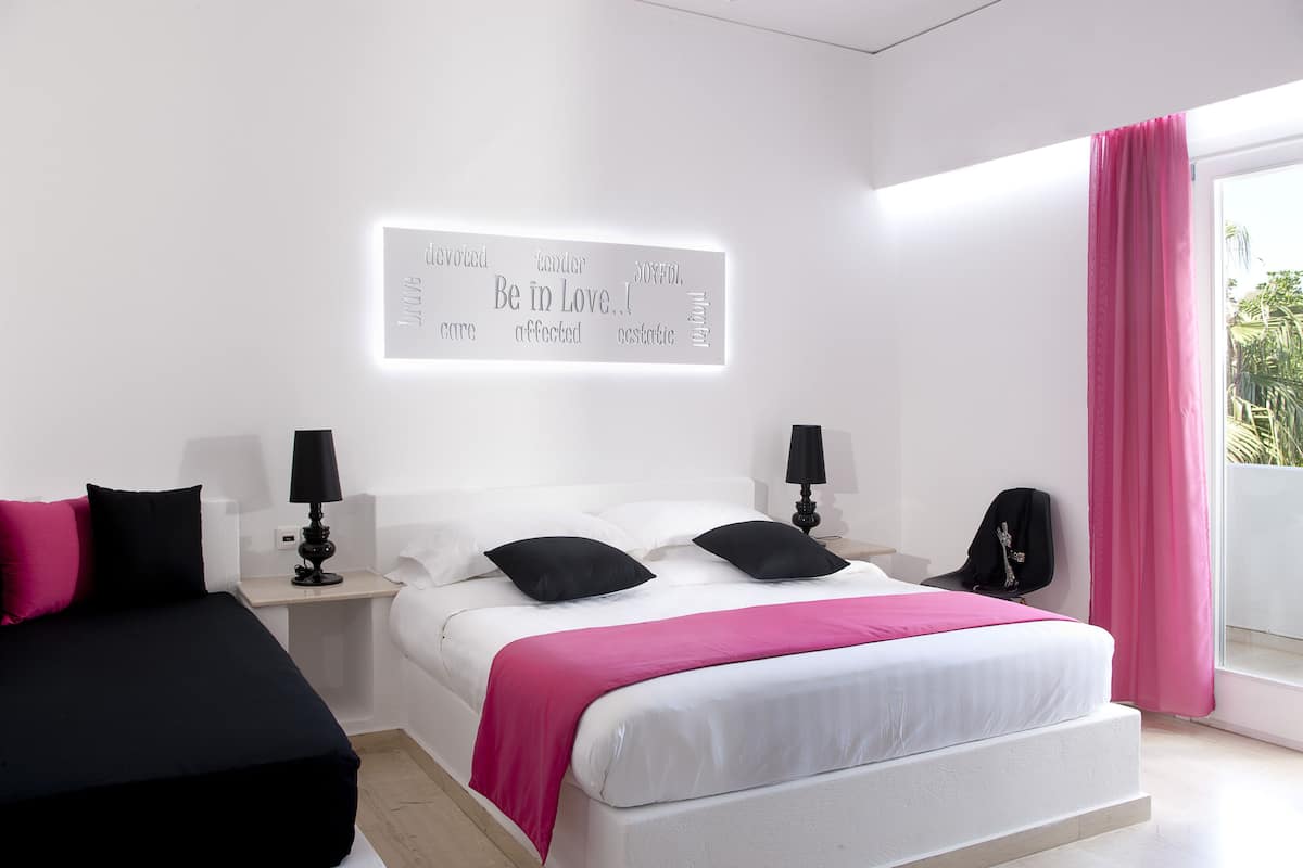 Une chambre moderne avec un lit, des tables de chevet, une lampe fixée au mur et une fenêtre avec des rideaux.