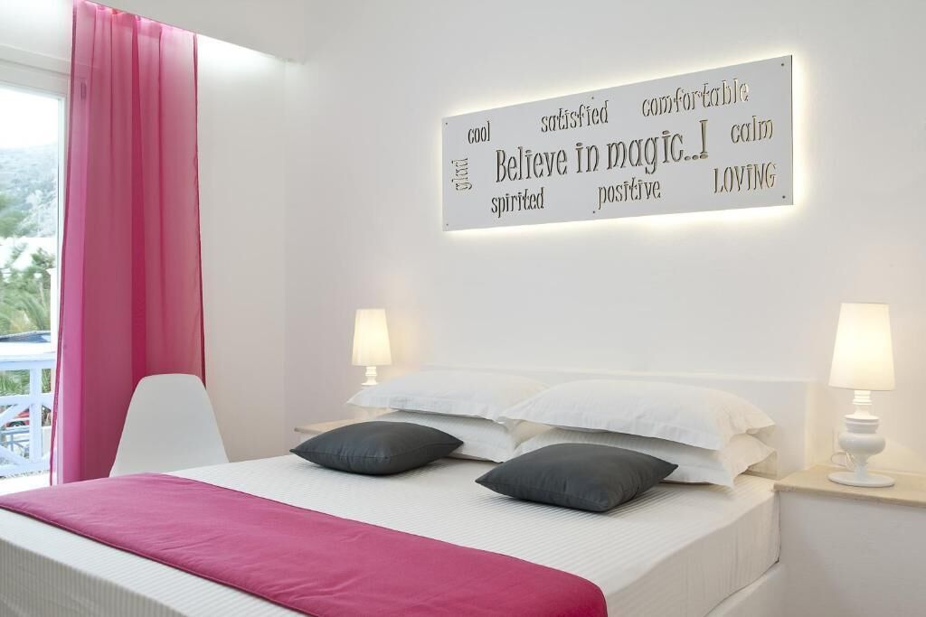 A hotel room with a bed, pillows, a nightstand, a lamp, and a wall sign with motivational words.