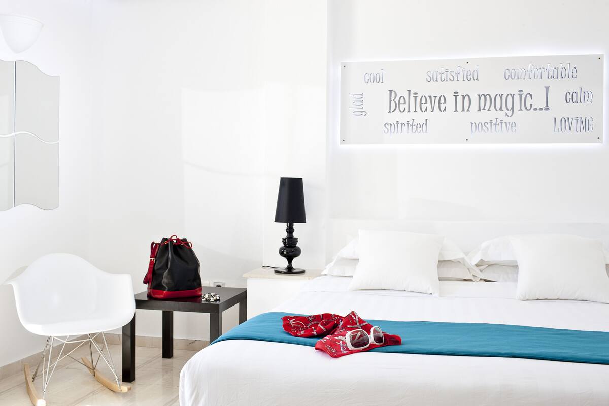 Une chambre d’hôtel bien rangée, avec un lit, une chaise, une table de chevet avec une lampe et une affiche motivante accrochée au mur.