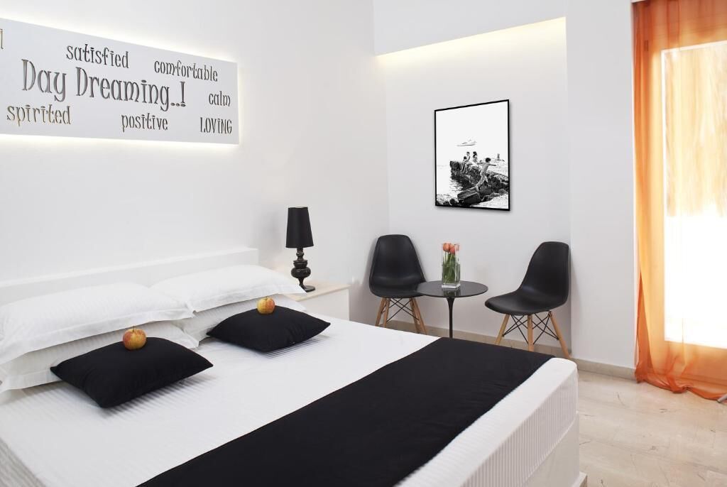 A modern hotel room with a neatly made bed, a side table with a lamp, two chairs, and a framed picture on the wall.