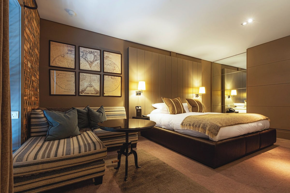 Une chambre d’hôtel moderne avec un grand lit, un canapé, une petite table et un miroir.